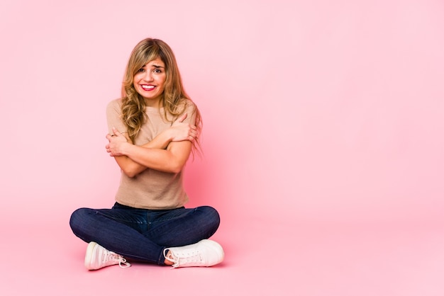 Giovane donna caucasica bionda che si siede su uno studio rosa che va freddo a causa della bassa temperatura o di una malattia.