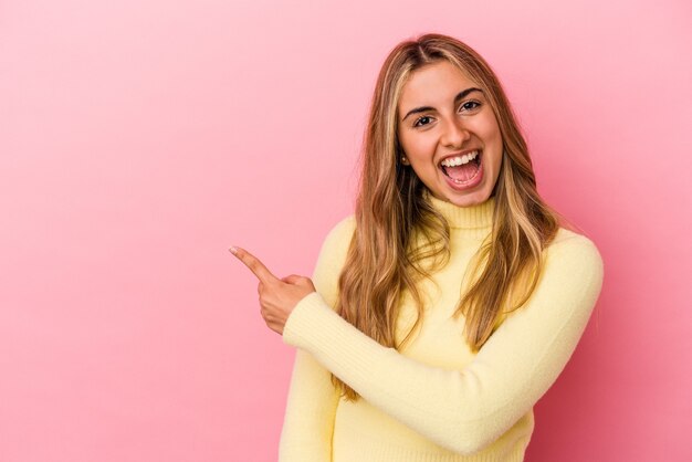 Young blonde caucasian woman  smiling and pointing aside, showing something