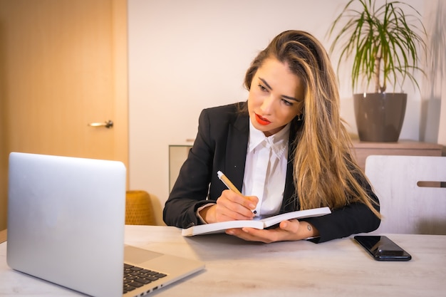 Young blonde Caucasian woman taking notes at online video call meeting