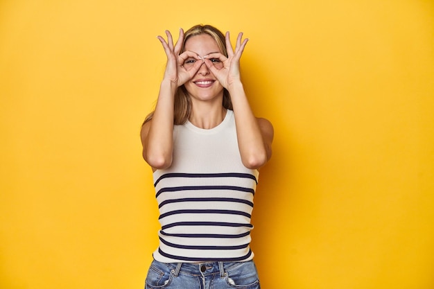 Photo young blonde caucasian woman in a white tank top on a yellow studio background