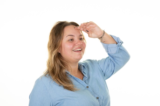 Young blonde curvy woman with hand on forehead in cap to see far or protect herself from the sun light on white background