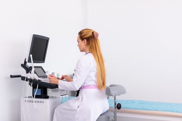 Young blonde doctor working on ultrasound machine in new clinic. Healthcare concept