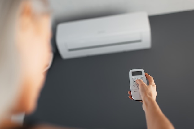 Young blonde female holds remote control of the air conditioner