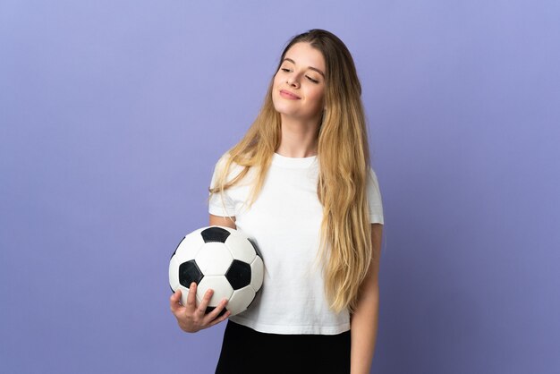 Young blonde football player woman isolated on purple wall looking to the side and smiling