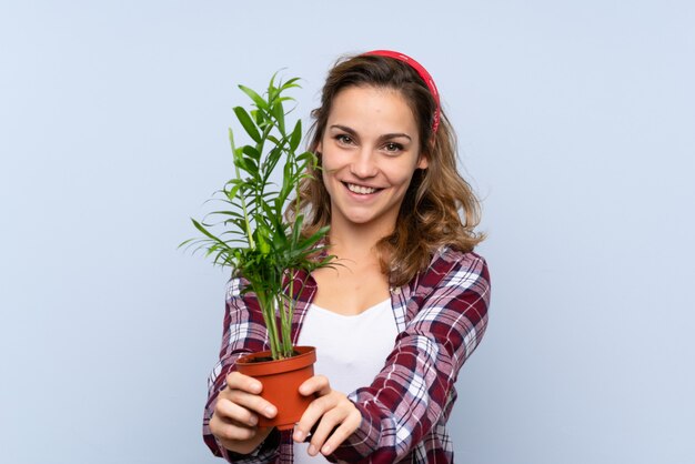 고립 된 파란색 벽 위에 식물을 들고 젊은 금발의 정원사 소녀