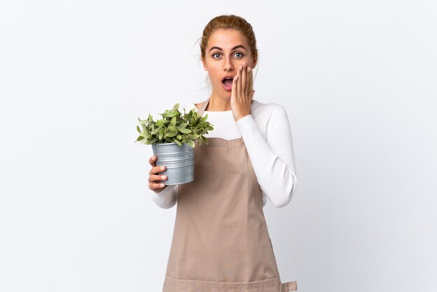 Photo young blonde gardener woman woman holding a plant over isolated white space with surprise facial expression