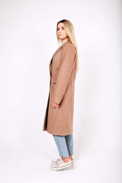 Young blonde girl in beige coat on white