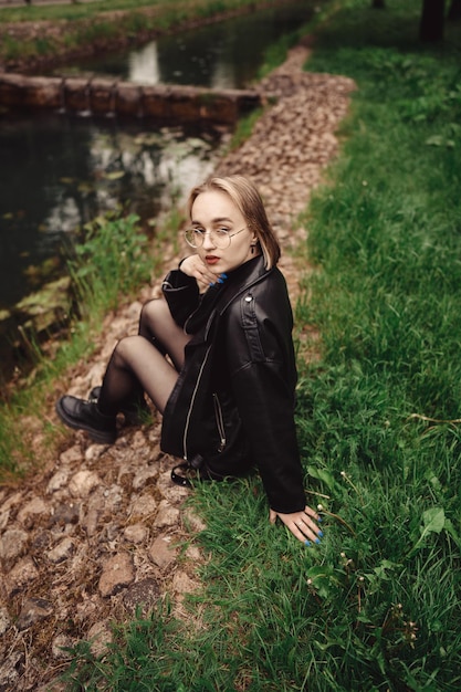 Young blonde girl in black is walking in the park alone and resting on the river's beach in autumn.