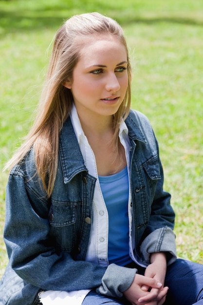 Young blonde girl looking towards the side while sitting down in a park