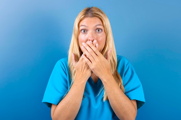 Young blonde girl nurse scared covering her mouth with her hands Concept fear