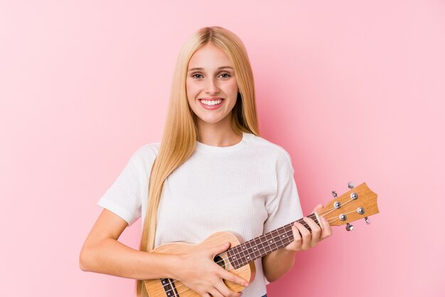 Young blonde girl playing ukelele happy, smiling and cheerful.