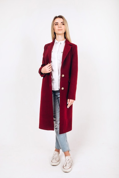 Young blonde girl in a red coat on a white 