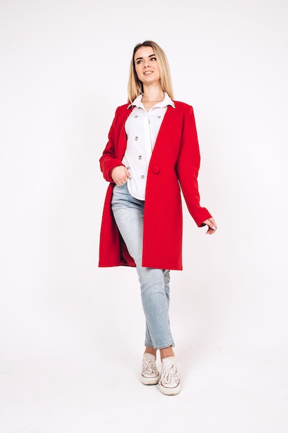 Young blonde girl in a red coat on a white 