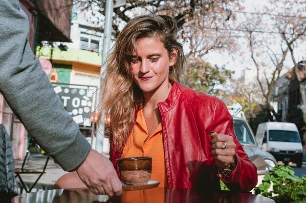 Young blonde girl sitting outside happy and smiling as she is served a cup of coffee at the table