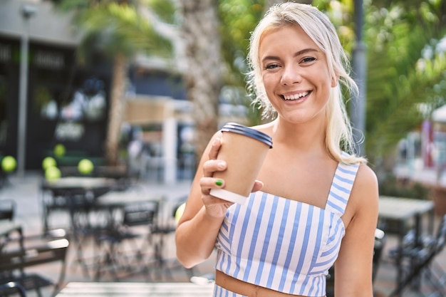 街でコーヒーを飲んで幸せな笑みを浮かべて若いブロンドの女の子