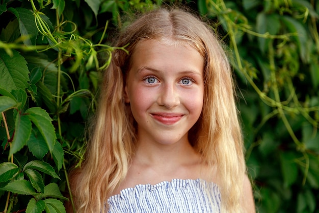 A young blonde girl stands in the leaves of wild grapes. High quality photo