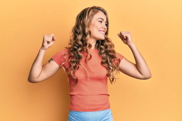 Young blonde girl wearing casual clothes showing arms muscles smiling proud. fitness concept.