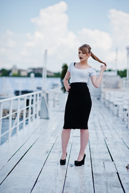 Young blonde girl with black lips on black skirts and white shirt posed on the pier