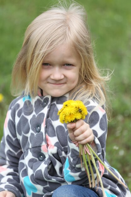 緑の芝生にタンポポの束を持つ若いブロンドの女の子