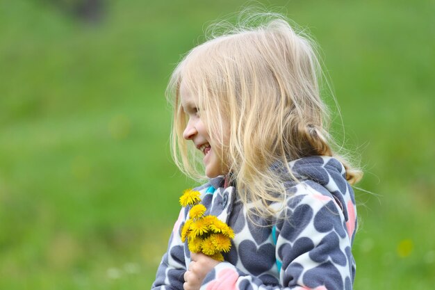 緑の芝生にタンポポの束を持つ若いブロンドの女の子