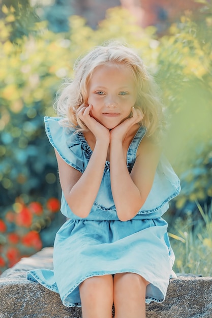 Young blonde girl with curly hair sits in the park in summer. High quality photo