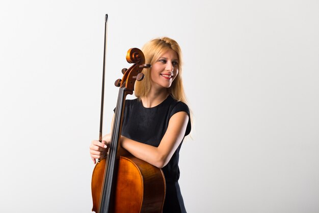 Young blonde girl with her cello posing on white wall