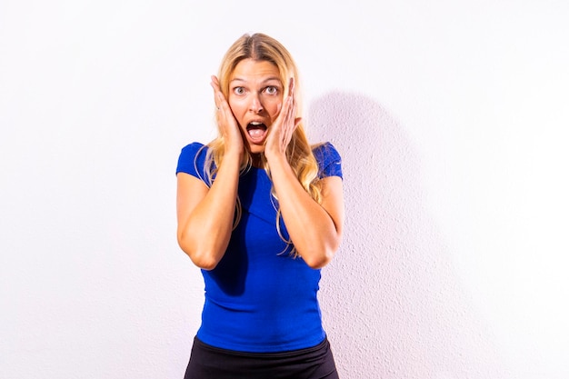 Young blonde girl with her hands on her face scared and looking at the camera White copy space