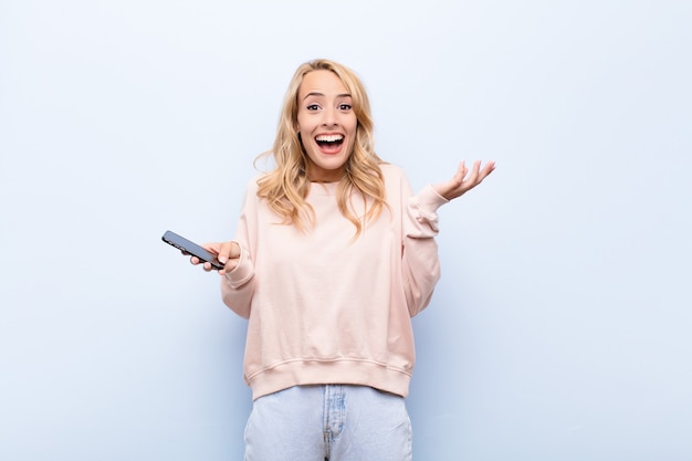 young blonde girl with smartphone feeling surprised and cheerful