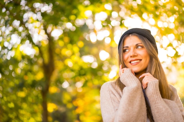 Young blonde girl with a wool cap in autumn at sunset in a natural park smiling