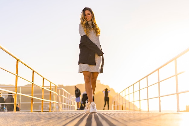 A young blonde in gray dress in a harbor on a beautiful orange sunset