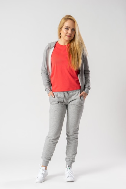 A young blonde in a gray tracksuit red tank top and white sneakers