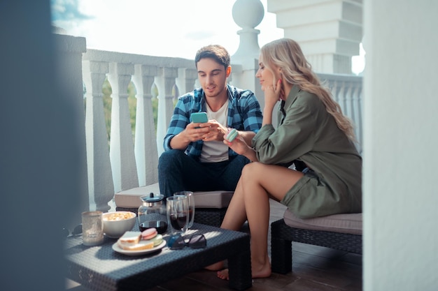 Young blonde-haired lady eating cookie and listening to man outdoors