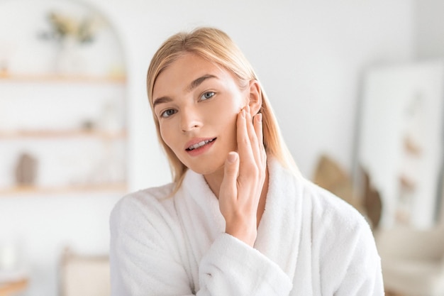 Young blonde lady examines and touches perfect face in bathroom