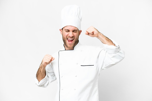 Giovane biondo chef su sfondo bianco isolato che celebra una vittoria