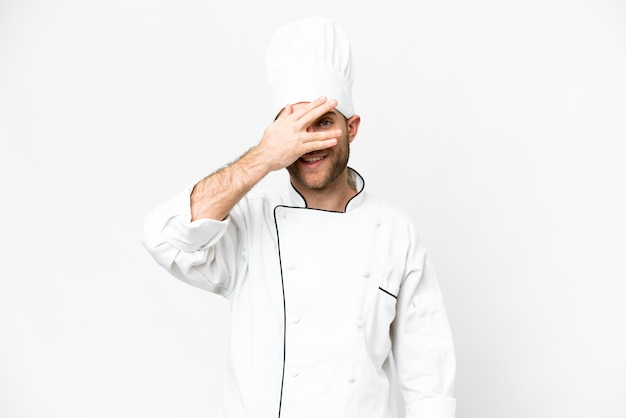 Young blonde man Chef over isolated white background covering eyes by hands and smiling