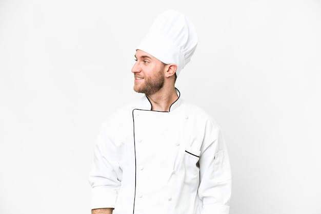 Young blonde man Chef over isolated white background looking side