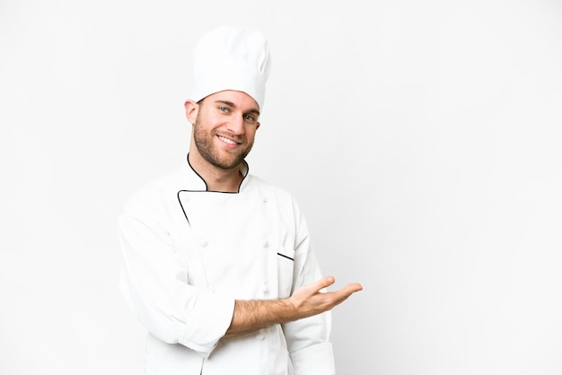 Young blonde man Chef over isolated white background presenting an idea while looking smiling towards