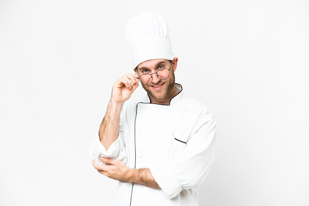 Young blonde man Chef over isolated white background with glasses and happy