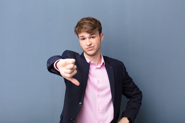 Young blonde man feeling displeased, showing thumbs down with a serious look