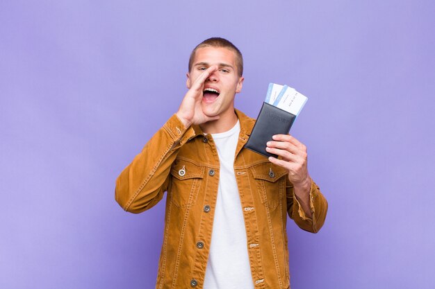 Young blonde man feeling happy, excited and positive, giving a big shout out with hands next to mouth, calling out