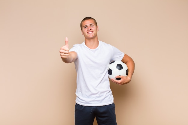 Young blonde man feeling proud, carefree, confident and happy, smiling positively with thumbs up