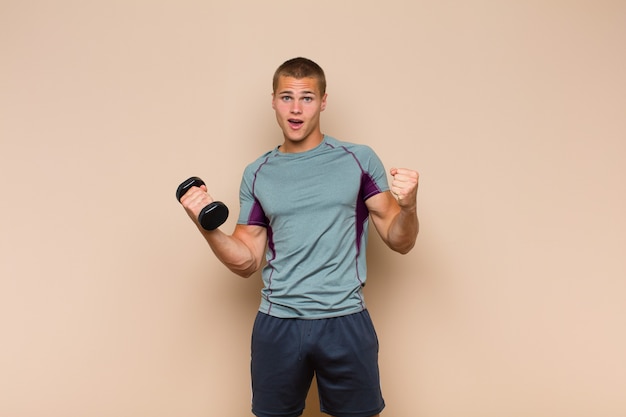 Young blonde man feeling shocked, excited and happy, laughing and celebrating success, saying wow!