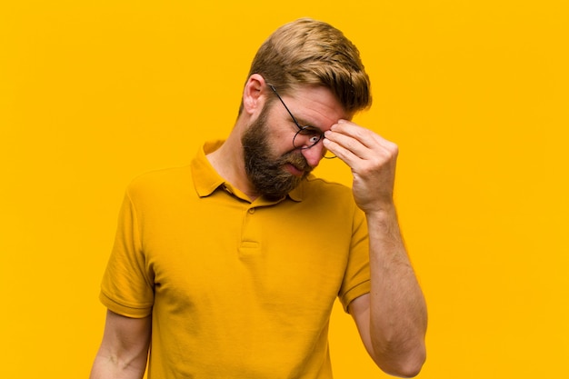 Young blonde man feeling stressed, unhappy and frustrated, touching forehead and suffering migraine of severe headache