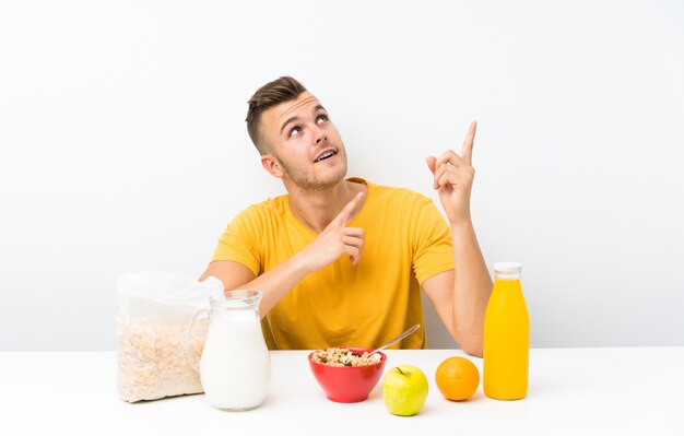 Young blonde man having breakfast pointing with the index finger a great idea