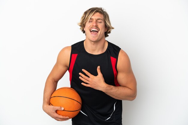 Young blonde man holding a ball of basketball isolated on white wall smiling a lot