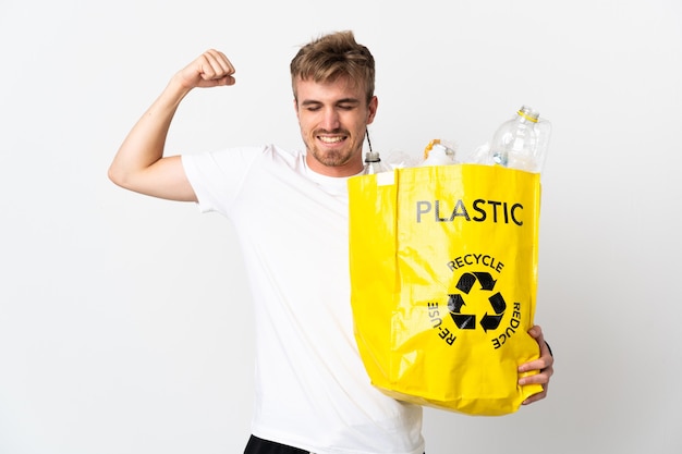 Young blonde man holding a recycling bag full of paper to recycle isolated on white background doing strong gesture