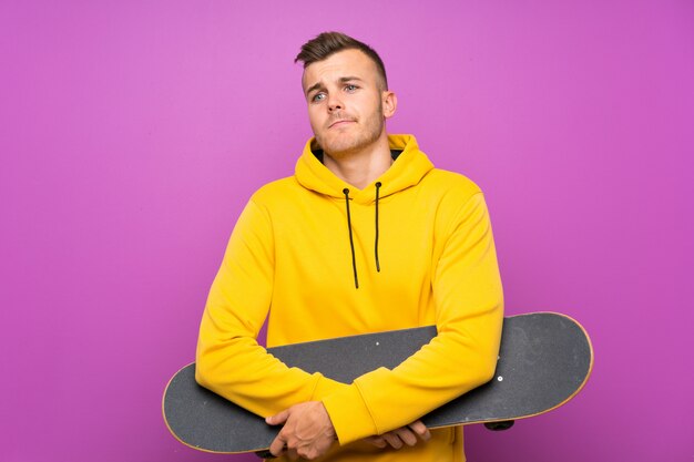 Young blonde man holding a skate making doubts gesture while lifting the shoulders