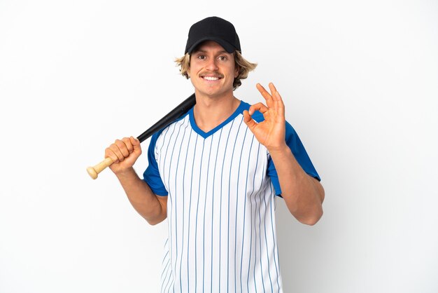 Giovane uomo biondo isolato su sfondo bianco giocando a baseball e mostrando segno ok con le dita