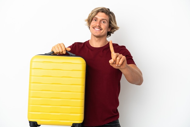 Young blonde man isolated on white background in vacation with travel suitcase and counting one