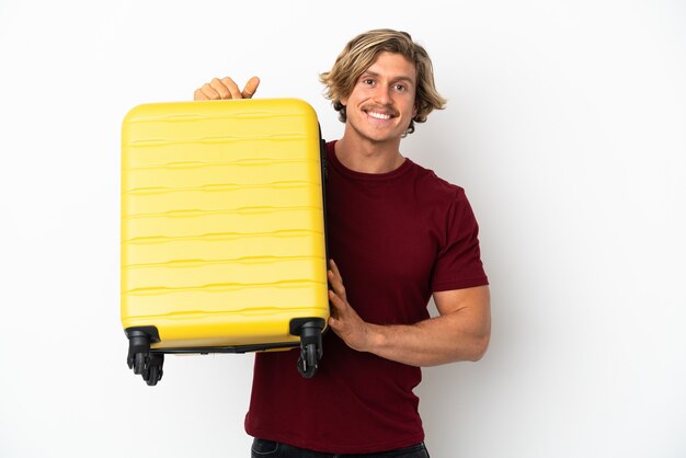 Young blonde man isolated on white wall in vacation with travel suitcase